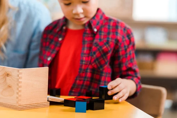 Foco seletivo de criança jogando blocos de construção ao lado do professor na escola montessori — Fotografia de Stock
