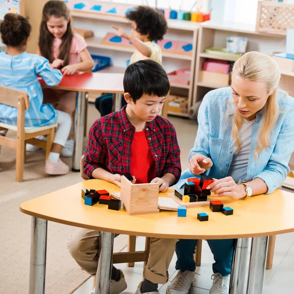 Focus selettivo di insegnanti e bambini che giocano con i bambini in background nella scuola montessori — Foto stock