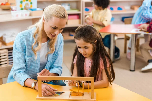 Focus selettivo del bambino e dell'insegnante che gioca al gioco di legno con i bambini in background nella scuola montessori — Foto stock