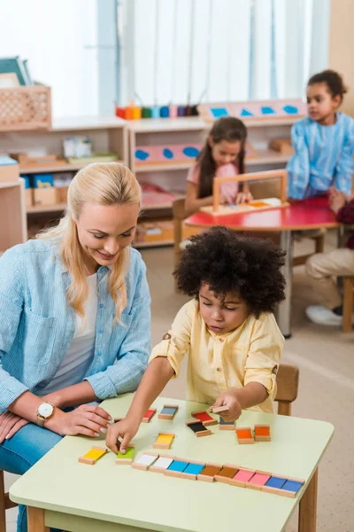 Foco seletivo do jogo infantil, sorrindo professor com crianças em segundo plano na escola montessori — Fotografia de Stock