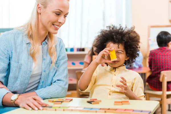 Foco seletivo de professor sorridente jogando jogo com criança afro-americana na classe montessori — Fotografia de Stock