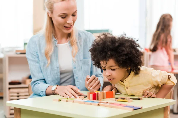 Focus selettivo del bambino afroamericano che gioca al gioco educativo con l'insegnante nella scuola montessori — Foto stock