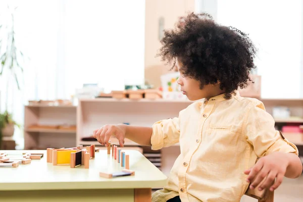 Vista lateral del niño afroamericano jugando a la mesa en la escuela montessori - foto de stock