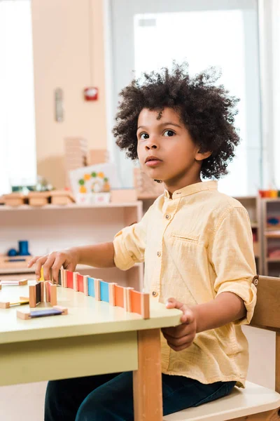 Pensiva criança afro-americana jogando jogo de madeira na escola montessori — Fotografia de Stock