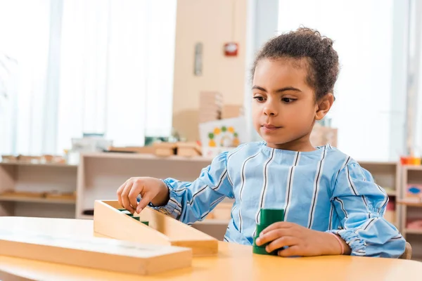 Focus selettivo del bambino afroamericano che gioca al gioco educativo in legno a tavola nella scuola montessori — Foto stock