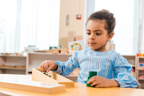 Concentration sélective d'un enfant afro-américain jouant à un jeu éducatif en bois à la table de l'école montessori — Photo de stock