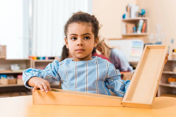 Focus selettivo del bambino afroamericano con gioco in legno e insegnante con bambini sullo sfondo nella scuola montessori — Foto stock