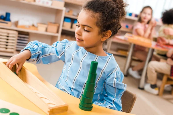 Foco seletivo da criança jogando jogo educativo com crianças em segundo plano na classe montessori — Fotografia de Stock