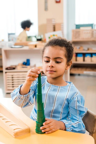 Enfoque selectivo del niño afroamericano con juego educativo en la mesa en la escuela montessori - foto de stock
