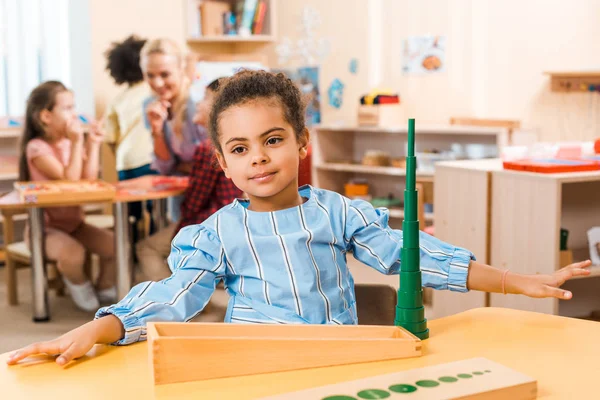 Selective focus of child with game and teacher with kids at background in montessori school — Stock Photo