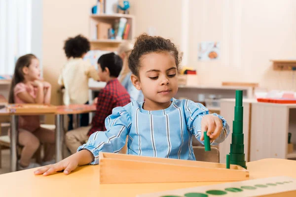 Focus selettivo del bambino che gioca al gioco educativo a tavola con i bambini sullo sfondo nella scuola montessori — Foto stock