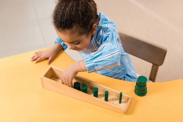 Vista aérea del niño afroamericano jugando juego de madera en la mesa en la escuela montessori - foto de stock