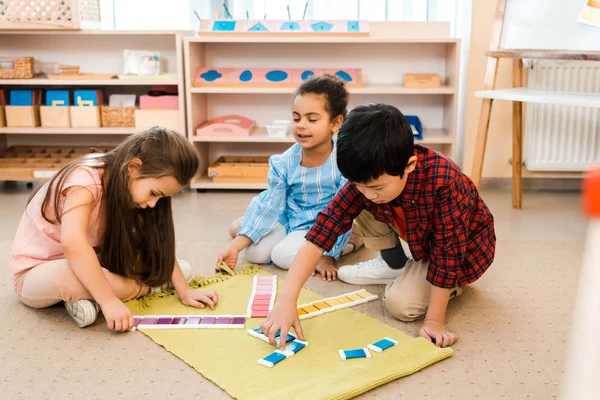 Дети играют в развивающую игру на полу в школе Монтессори — стоковое фото