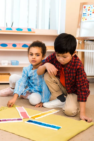 Bambini che giocano con gioco colorato su tappeto in classe montessori — Foto stock