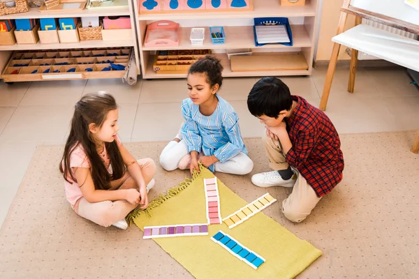 Vue grand angle des enfants jouant au jeu assis sur le sol dans la classe montessori — Photo de stock