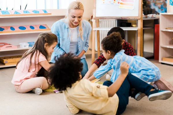 Focus selettivo di insegnanti e bambini che giocano sul pavimento nella scuola montessori — Foto stock