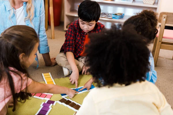 Focus selettivo di bambini pieghevole gioco colorato da insegnante sul pavimento nella scuola montessori — Foto stock