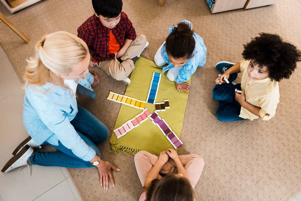 Вид сверху на учителя, играющего с детьми в развивающую игру на полу в классе Монтессори — стоковое фото