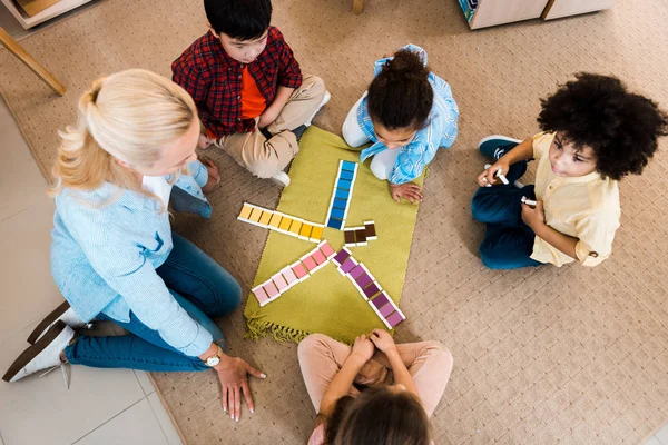 Overhead view of teacher playing with kids educational game on floor in montessori class — Stock Photo
