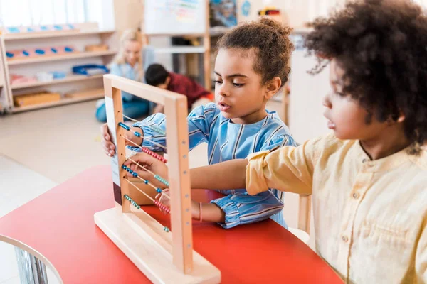 Focus selettivo dei bambini afroamericani che giocano con punteggi con insegnante e bambino sullo sfondo nella scuola montessori — Foto stock