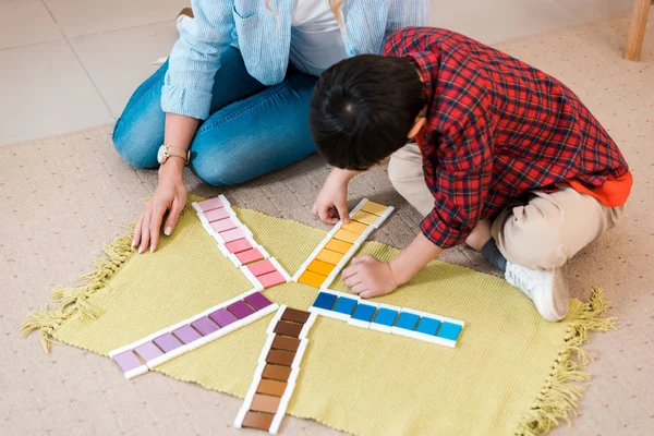 Vista de ángulo alto del maestro y el niño jugando colorido juego en el suelo en la escuela montessori - foto de stock