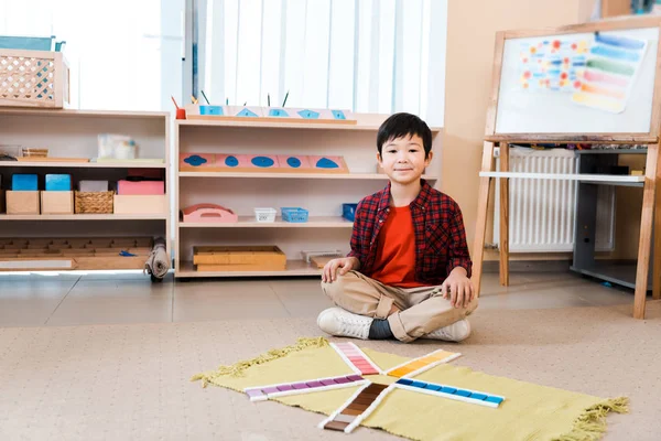 Sorridente asiatico bambino guardando macchina fotografica da educativo gioco su pavimento in montessori scuola — Foto stock