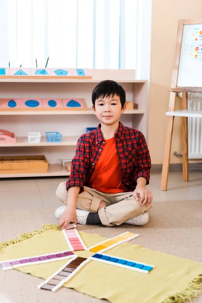 Kind schaut in Kamera beim Lernspiel auf dem Fußboden in Montessori-Schule — Stockfoto