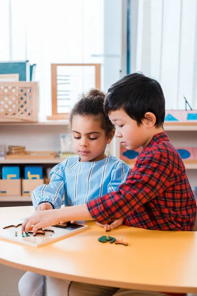 Niños jugando juego educativo en la mesa en clase montessori - foto de stock