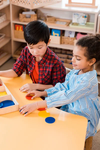 Vista de ángulo alto de los niños plegando juego colorido durante la lección en la escuela montessori - foto de stock