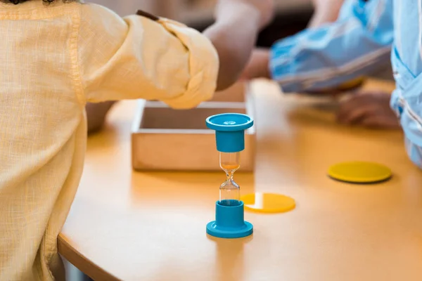 Селективное внимание детей с образовательной игрой и песочными часами за столом в школе Монтессори — стоковое фото