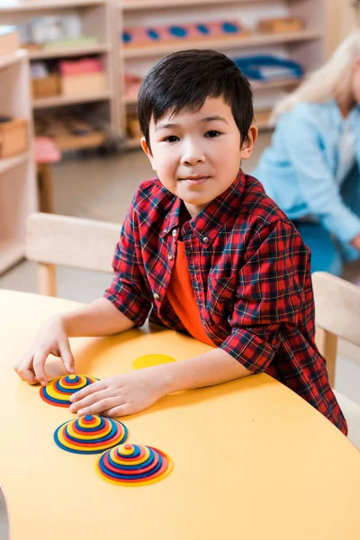 Selective focus of asian kid looking at camera while playing at desk in montessori school — Stock Photo