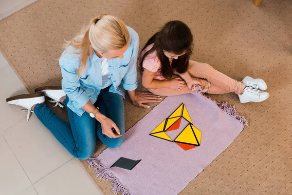 Overhead view of teacher and kid sitting on floor by colorful game in montessori class — Stock Photo
