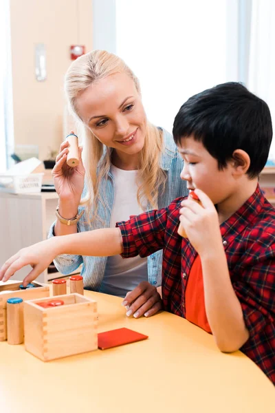 Selective focus of smiling teacher looking at asian kid during lesson in montessori school — Stock Photo