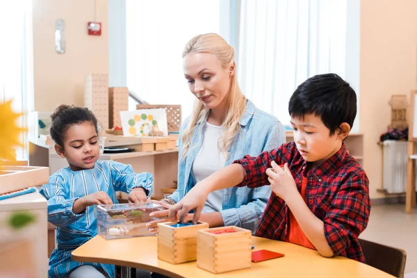 Concentration sélective des enfants jouant à des jeux éducatifs par le professeur à l'école montessori — Photo de stock