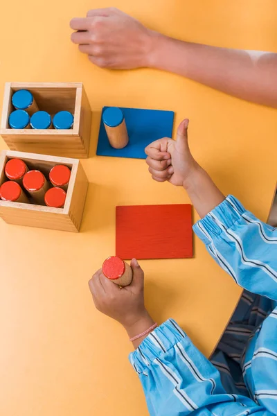 Vue grand angle de l'enfant montrant pouce levé par jeu en bois et professeur à l'école montessori, vue recadrée — Photo de stock