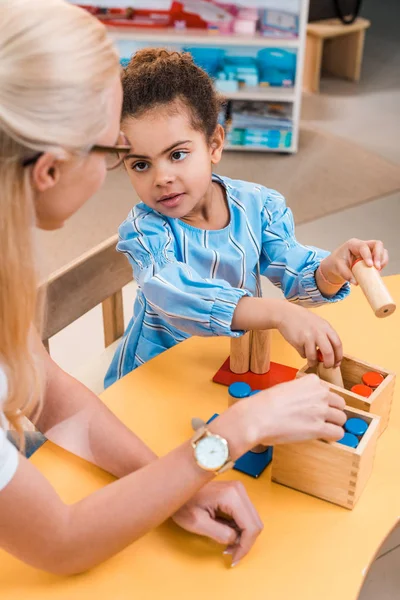 Concentration sélective de l'enfant avec jeu en bois en regardant le professeur dans la classe montessori — Photo de stock