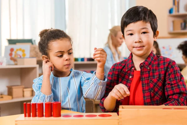 Concentration sélective des enfants avec jeu de société au bureau avec professeur et enfants en arrière-plan dans la classe montessori — Photo de stock