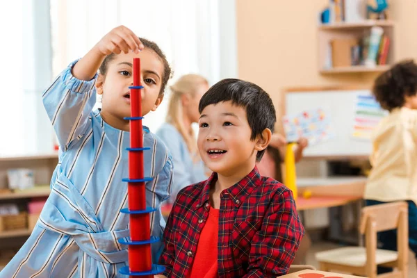 Foco seletivo de crianças jogando jogo educativo com professor e criança em segundo plano na classe montessori — Fotografia de Stock