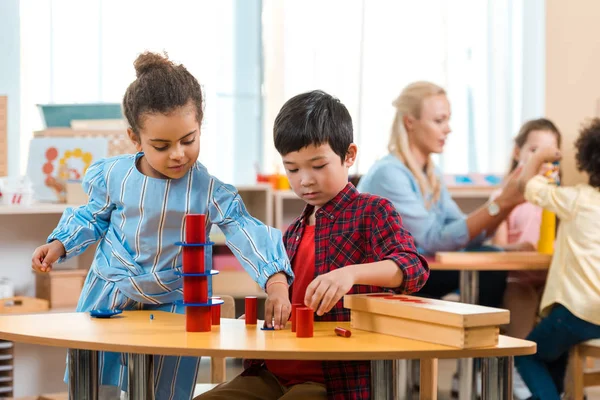 Concentration sélective des enfants pliant jeu éducatif avec l'enseignant et les enfants en arrière-plan à l'école montessori — Photo de stock