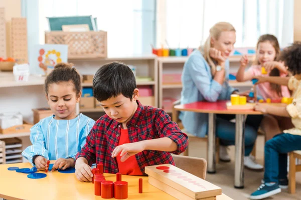 Selective focus of kids playing games with children and teacher at background in montessori school — Stock Photo