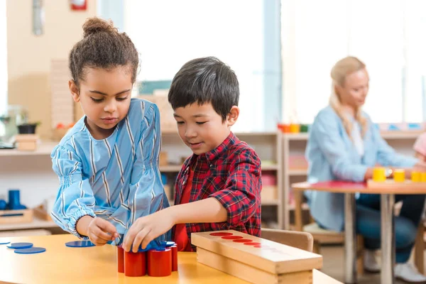 Concentration sélective des enfants pliant jeu éducatif avec professeur en arrière-plan dans la classe montessori — Photo de stock