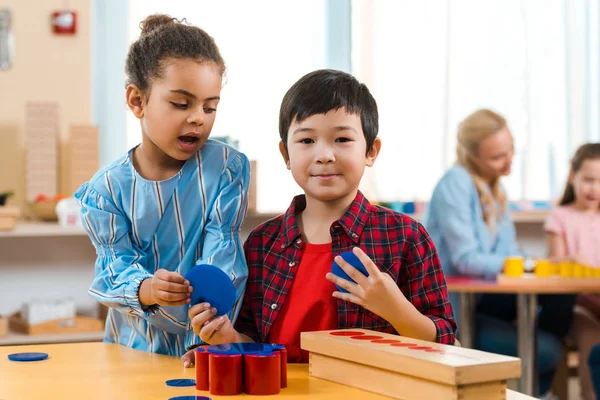 Foco seletivo de crianças com jogo educativo e professor com criança em segundo plano na aula de montessori — Fotografia de Stock