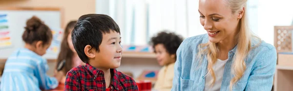 Panoramaaufnahme einer lächelnden Lehrerin und eines Kindes mit Kindern im Hintergrund in der Montessori-Schule — Stockfoto