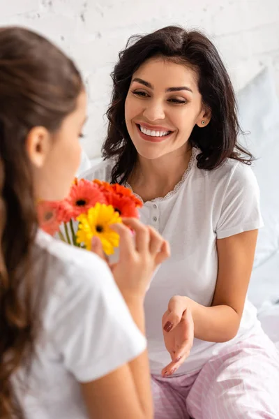 Happy woman looking at daughter holding bouquet of gerberas on mothers day — Stock Photo
