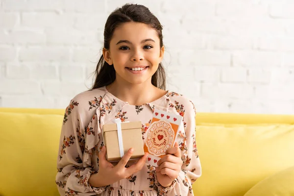 Cute, happy child in elegant dress holding gift box and mothers day card with i love you mommy inscription — Stock Photo