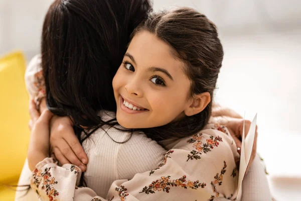 Adorable, niño feliz sonriendo a la cámara mientras abraza a la madre en el día de la madre - foto de stock