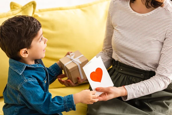 Adorabile ragazzo che presenta la scatola regalo e la carta di giorno delle madri con il simbolo del cuore alla mamma — Foto stock