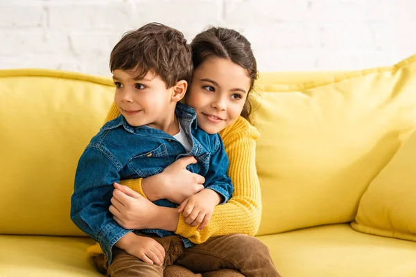 Happy child hugging adorable brother while sitting on yellow sofa at home — Stock Photo