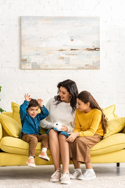 Enfants heureux et mère joyeuse assis sur le canapé avec lapin drôle blanc — Photo de stock