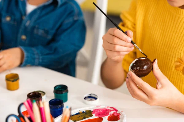 Vista cortada de criança pintando ovo de Páscoa enquanto sentado perto do irmão — Fotografia de Stock